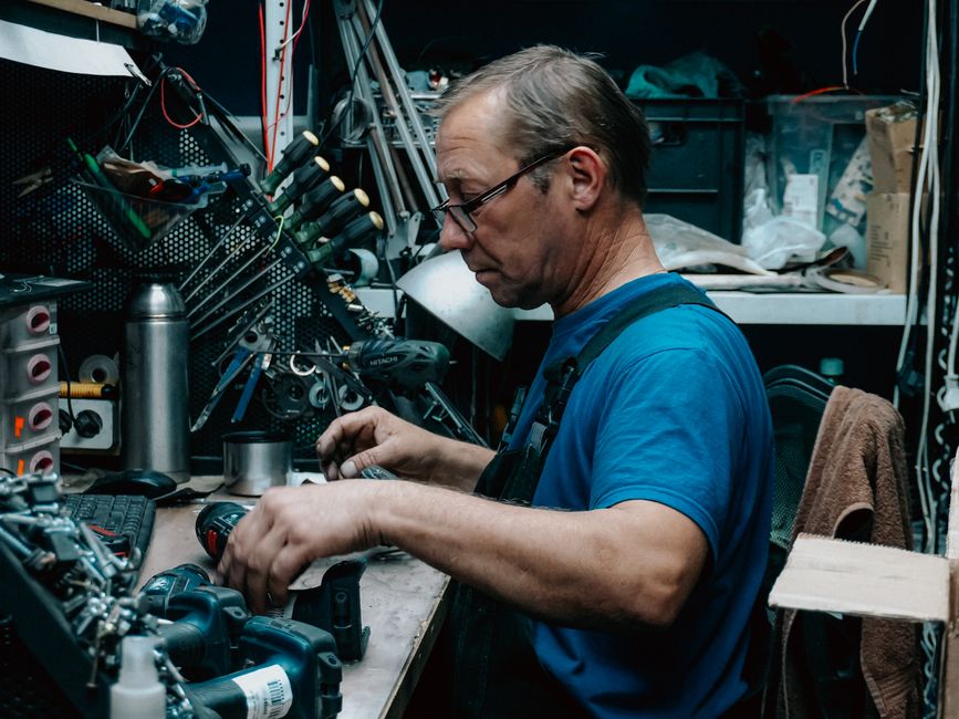A focused technician repairing equipment at a cluttered workbench in a workshop.