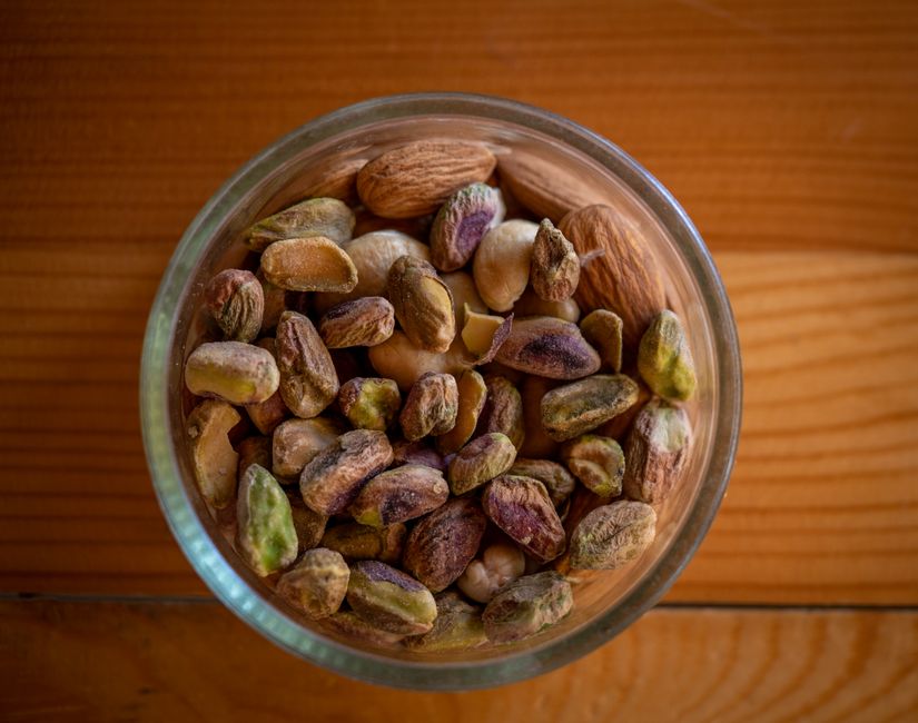 A close-up top view of assorted nuts in a glass bowl on a wooden table, highlighting natural textures.