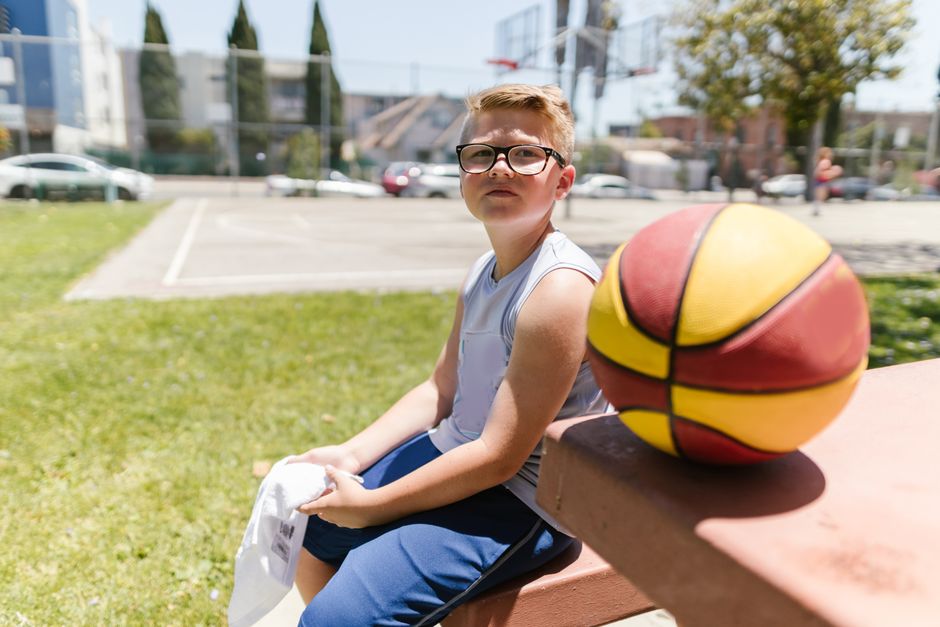 A young boy takes a break with a basketball on a sunny day outside.
