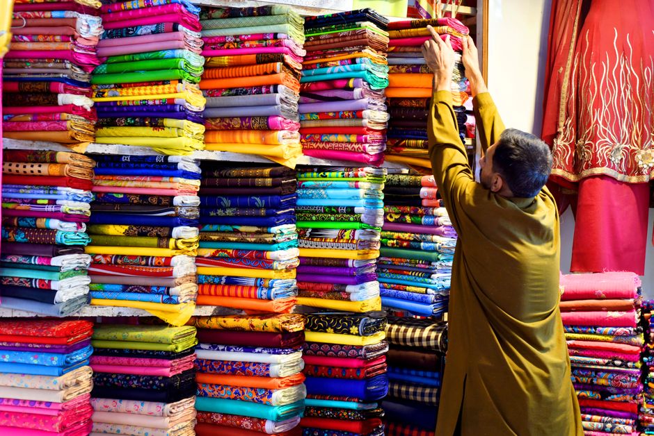 Colorful fabric stacks at a market in Multan, Pakistan, vendor arranging cloth.