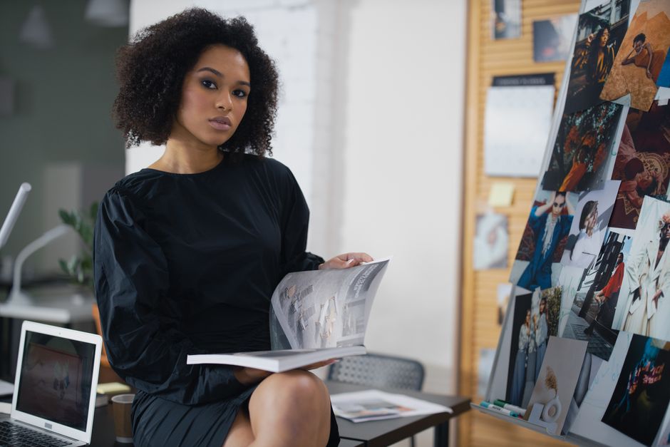 Elegant woman in a black dress holding a magazine in a modern office environment.