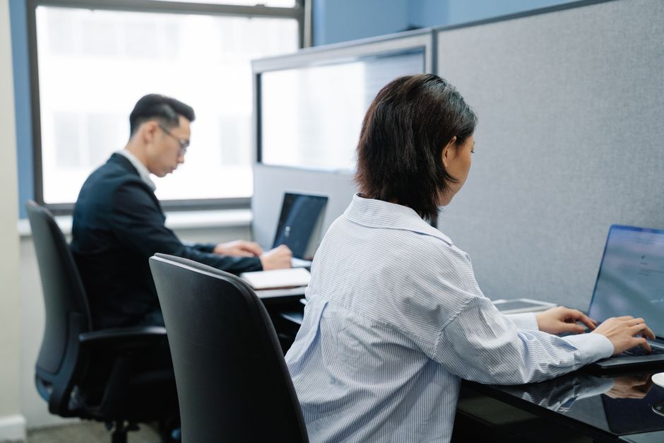 Two professionals working on laptops in a modern office cubicle setup.