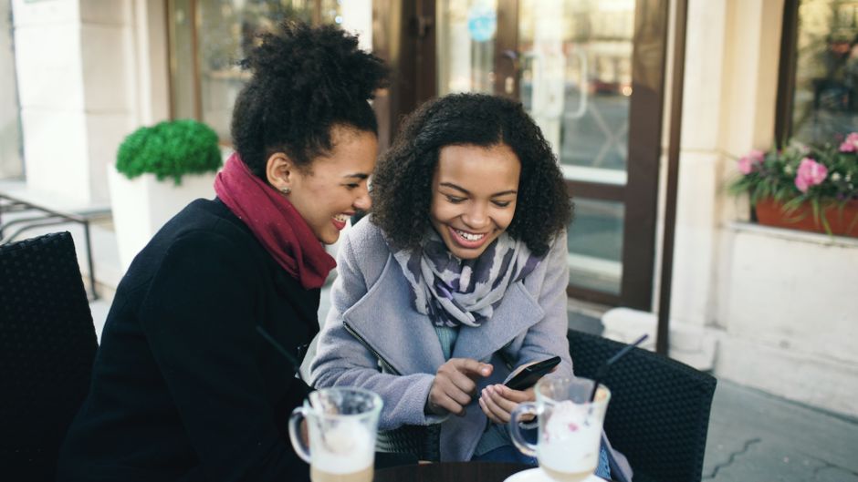 Two friends laughing over coffee at an outdoor cafe, sharing a joyful moment.