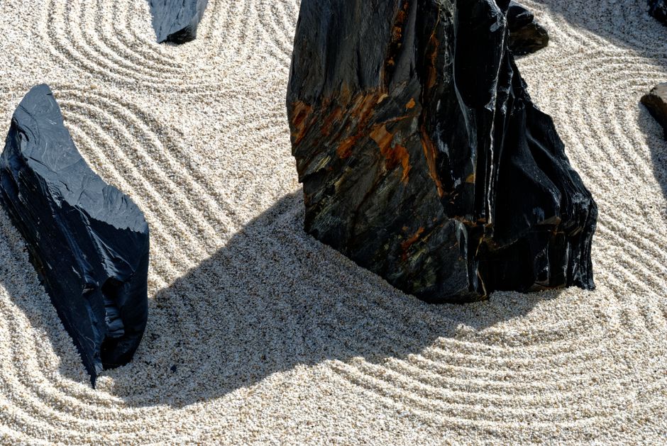 symbolizing mindfulness and relaxation Peaceful Zen garden scene featuring raked sand patterns around dark stones, evoking tranquility.