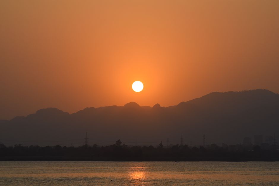 A peaceful Japanese tea ceremony – A person slowly pouring tea into a cup, symbolizing mindfulness and relaxation. Peaceful sunset view with sun setting over distant mountains and calm water surface.