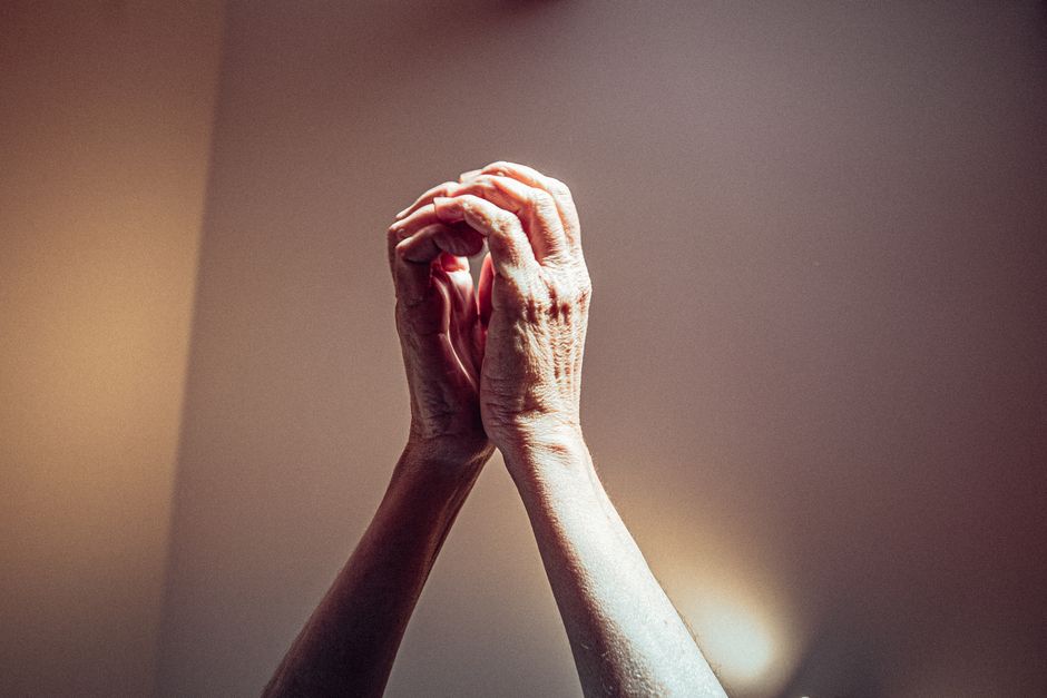 Close-up of elderly hands clasped in prayer with dramatic lighting highlighting wrinkles.