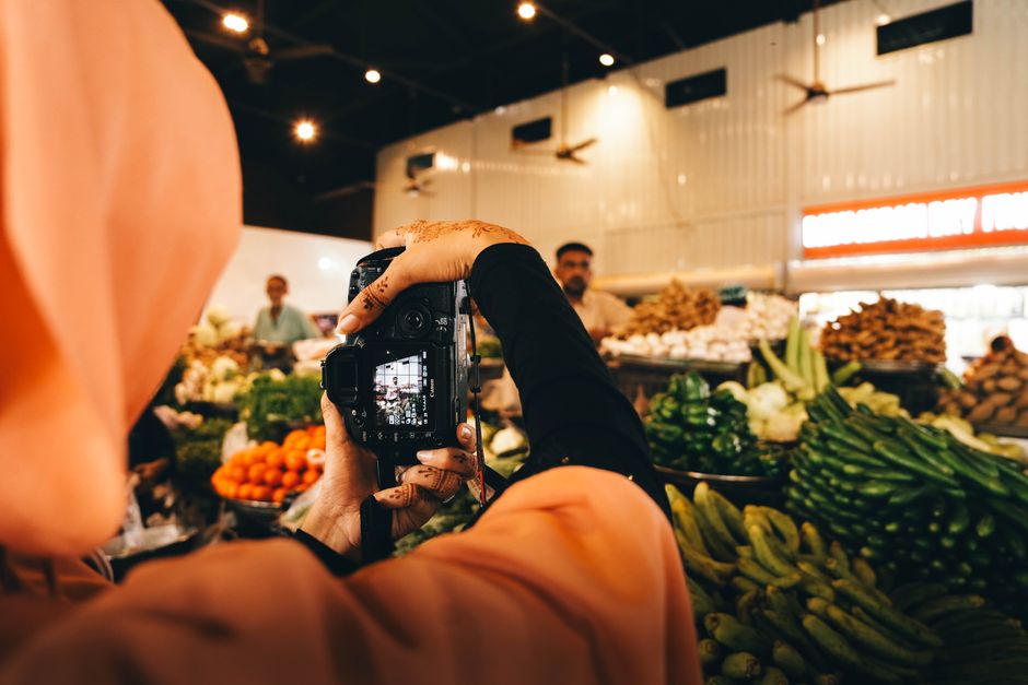 A woman photographer with henna captures vibrant vegetables at an indoor market in Sindh, Pakistan.