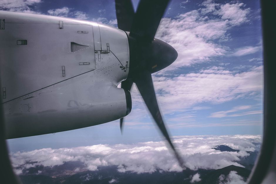 View through a propeller plane window, showcasing clouds and sky from above.