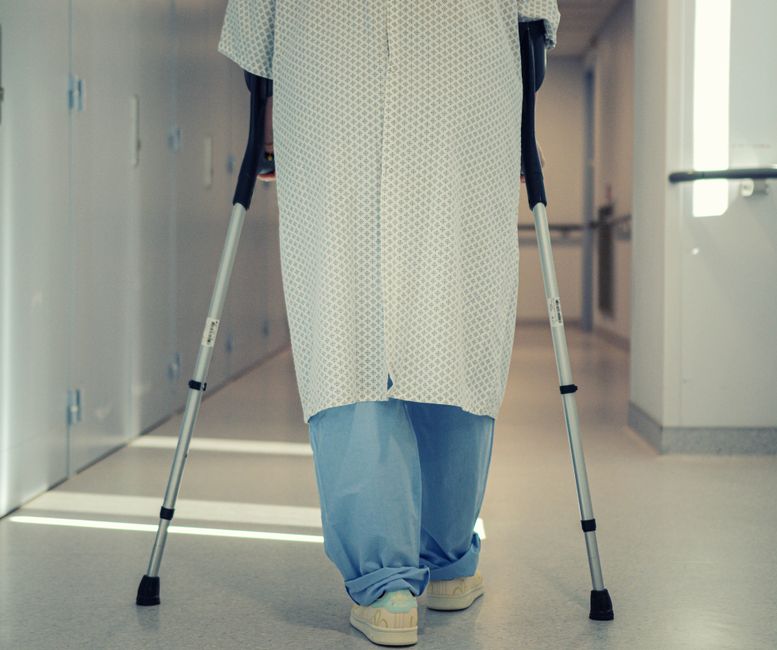 A senior patient using crutches to walk down a hospital corridor, symbolizing recovery and mobility assistance.