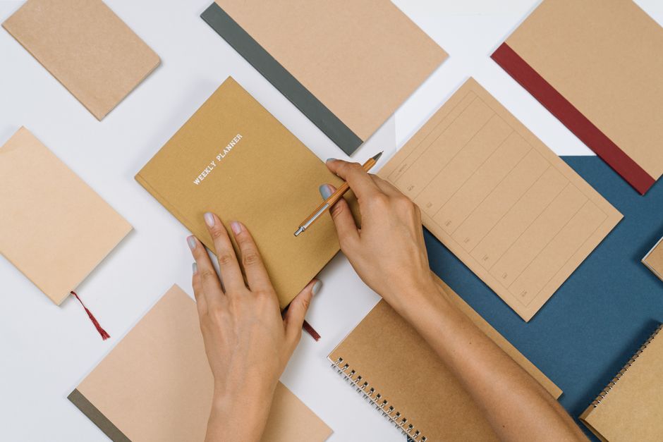 Organized flat lay of stationery items with hands writing in a planner, suitable for productivity themes.