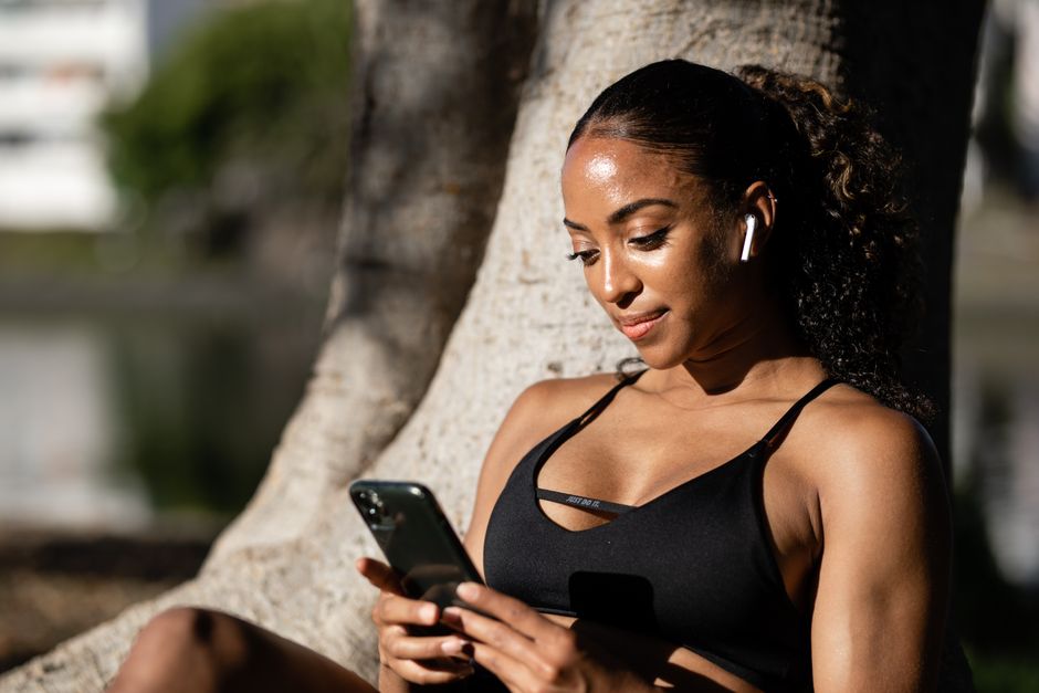 Woman in athletic attire using smartphone outdoors, enjoying a sunny day.