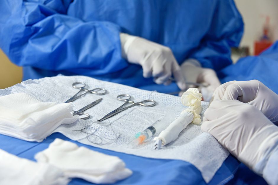 Detailed view of surgical instruments and hands in blue scrubs performing surgery.