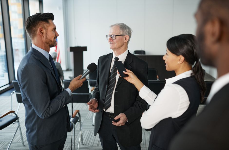 Journalists conduct an interview with a senior executive in a formal office setting.