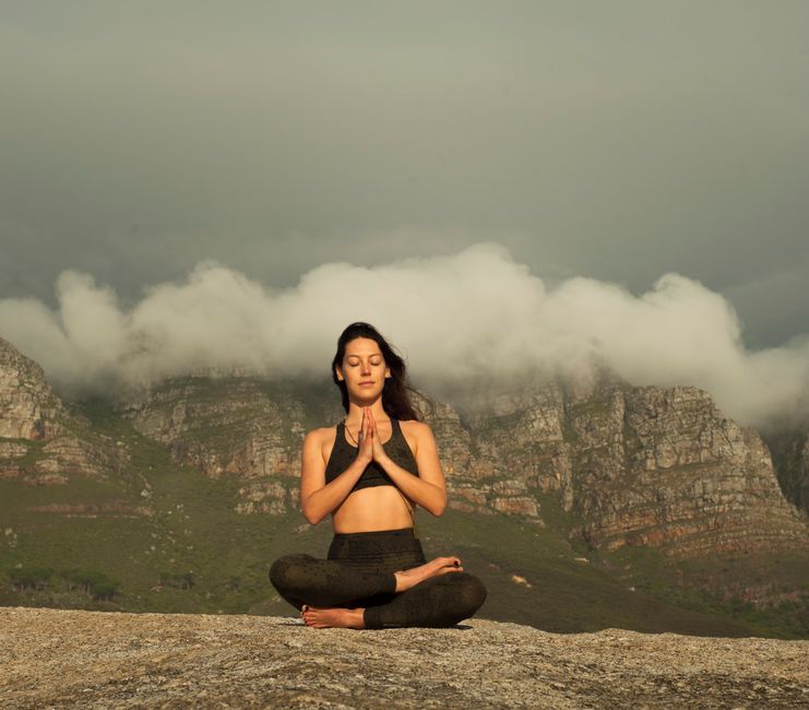 A woman practices yoga meditation outdoors in a serene mountain setting, promoting relaxation and wellness.