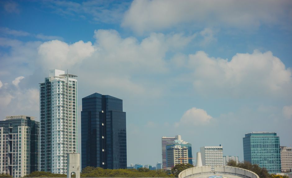 Urban skyline featuring modern skyscrapers beneath a bright blue sky with fluffy clouds.