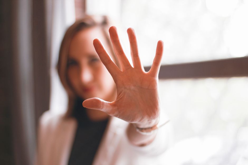 Close-up of a woman's hand gesturing stop with a blurred background indoors.