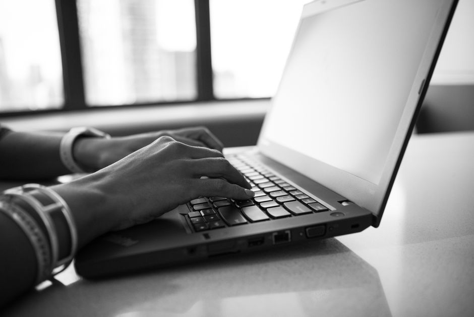 Close-up black and white photo showing hands typing on a laptop, emphasizing modern technology.