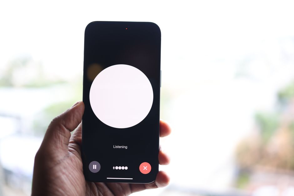 Close-up of a hand holding a smartphone displaying a voice assistant interface.