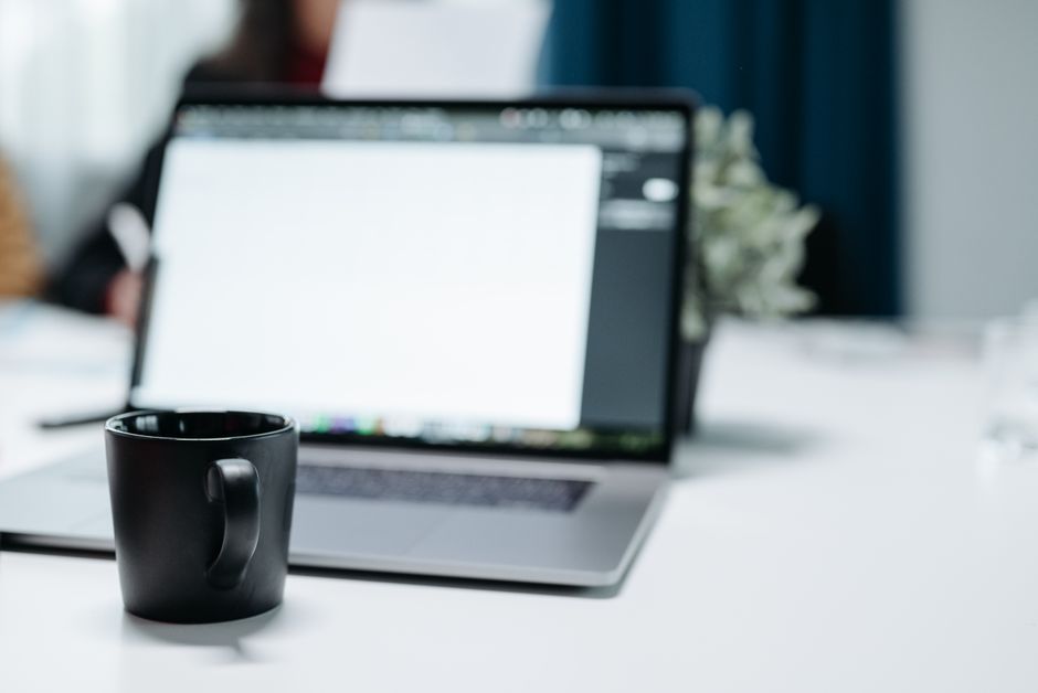 A black coffee mug on an office desk with a blurred laptop in the background.