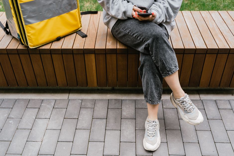 A courier taking a break outdoors with a yellow thermal bag, sitting on a wooden bench.