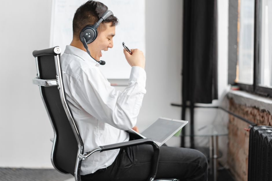Professional man expressing excitement during a virtual meeting. Indoors, using a headset and laptop.