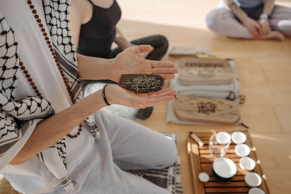 A peaceful indoor meditation session featuring herbal ceremony tools and participants engaged in alternative therapy.