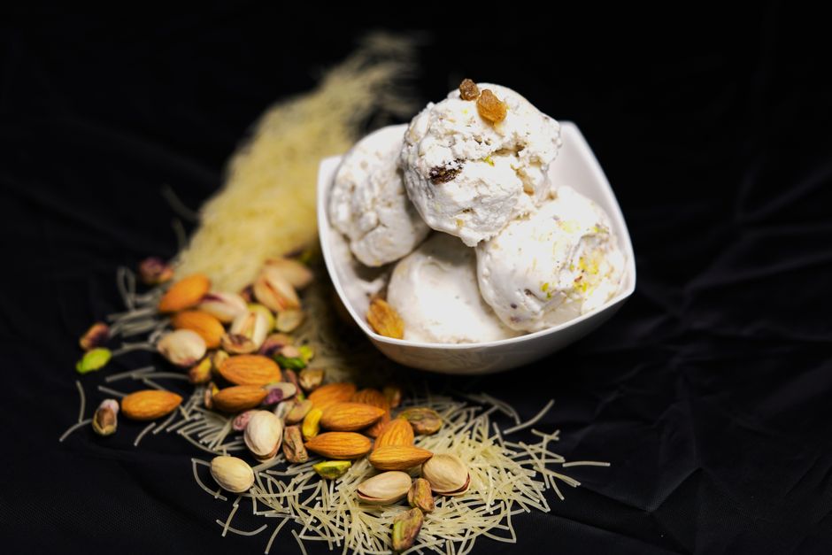 Creamy kulfi in a bowl with assorted nuts and vermicelli on a dark background.