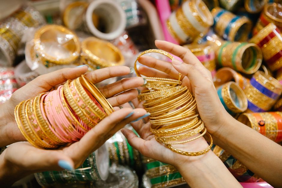 Vibrant close-up of hands displaying intricate golden bangles in a busy market setting.