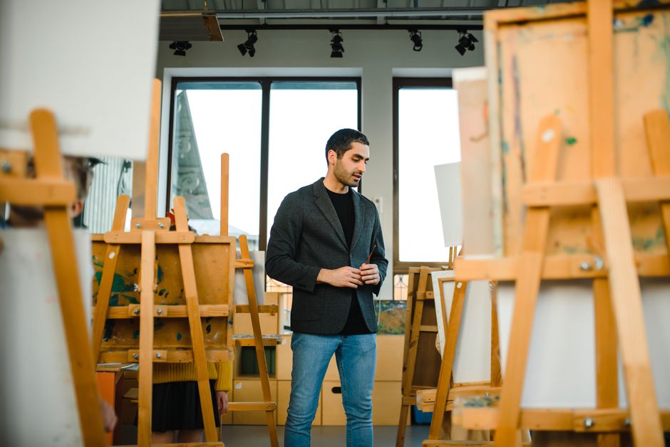 Young artist surrounded by easels in a contemporary art studio setting.