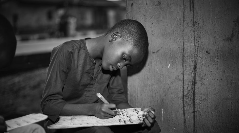 Black and white image of a young boy writing on a slate, focused and determined.