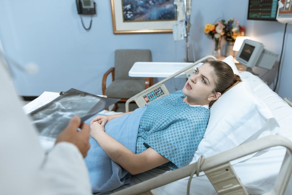 Caucasian woman in hospital bed receiving care from healthcare professional.