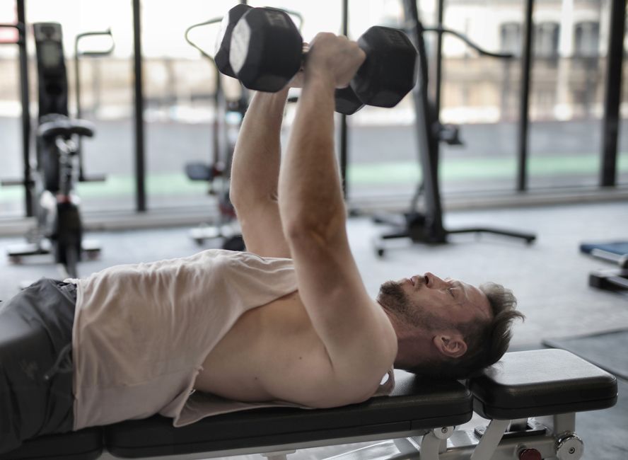 Diet Man performing dumbbell press on bench indoors, focusing on muscle strength.
