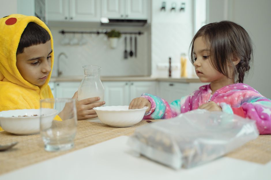 Two children enjoying breakfast together in colorful costumes at home.