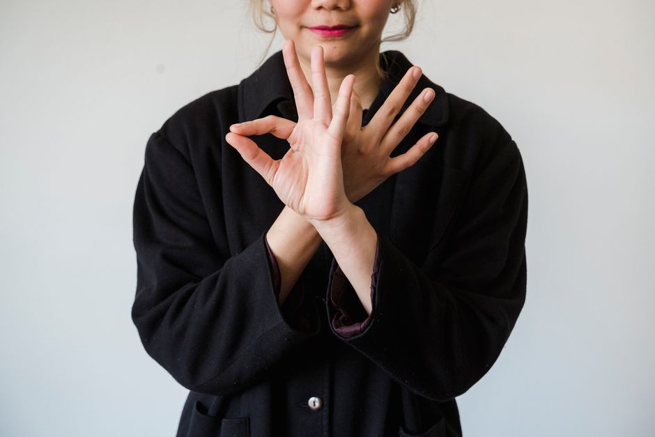 A person in a black jacket making unique hand gestures against a white background.