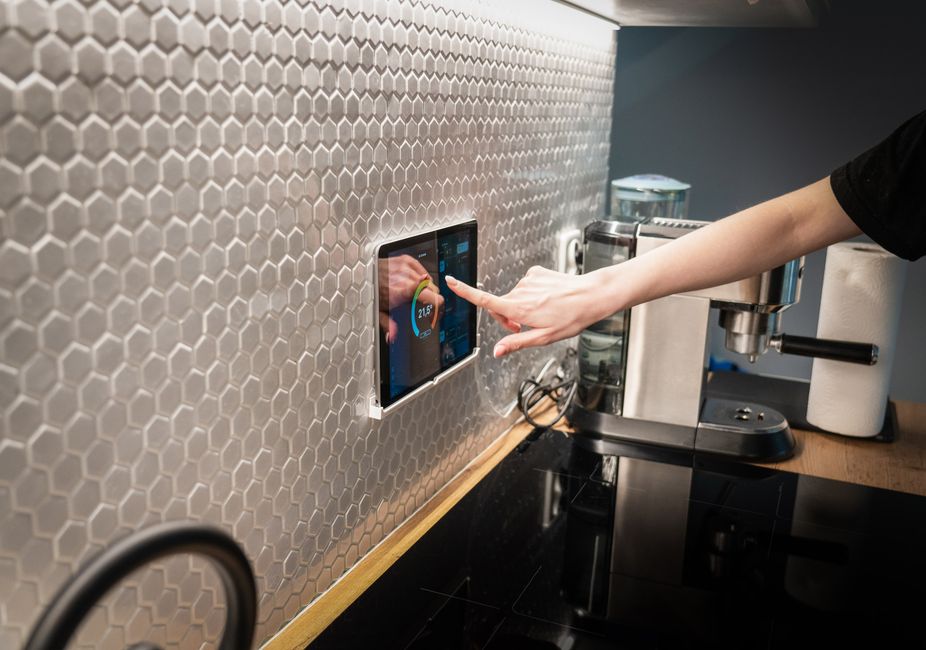A modern kitchen with a touchscreen smart home control panel integrated into a hexagon-patterned wall.
