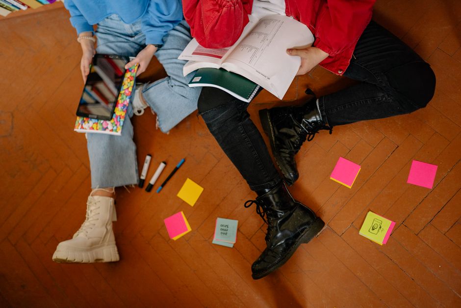 Two students studying on the floor with books, tablets, and colorful sticky notes.