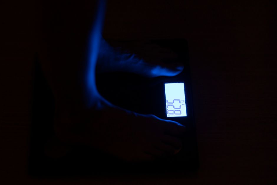 Close-up of a digital weighing scale displaying weight in a dark room with blue illumination.