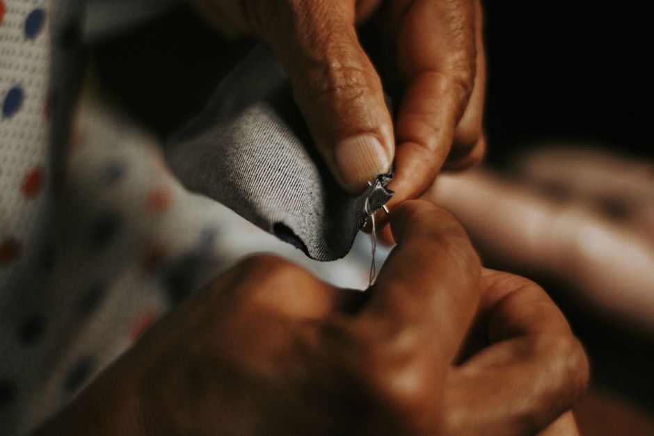 Close-up of adult hands sewing gray fabric thread and needle, showcasing craftsmanship.