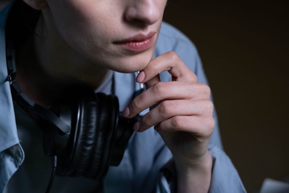 Close-up of a woman wearing headphones, deep in thought, hand touching chin.