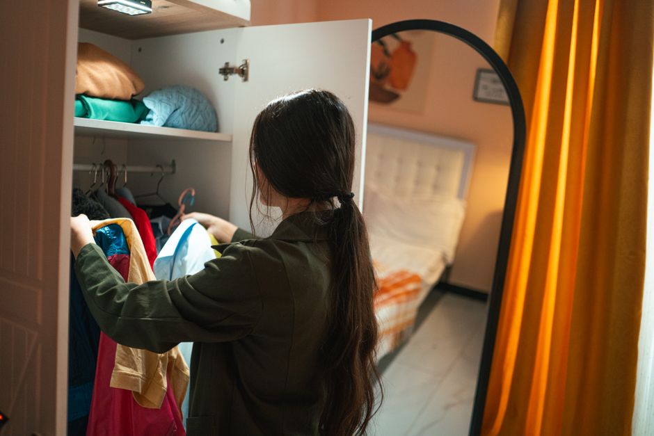 A woman organizes clothes in her wardrobe with a cozy bedroom setting.