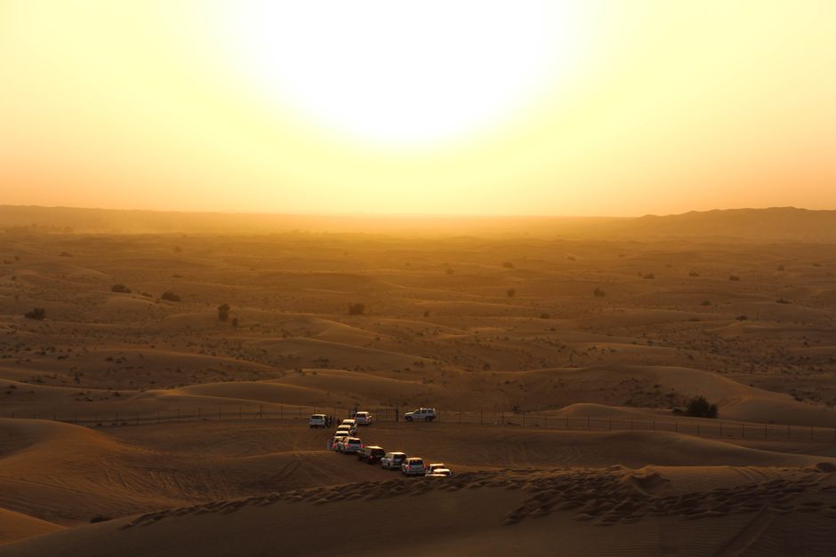 Off-road vehicles traverse the desert dunes under a warm golden sunset, ideal for adventure travel.