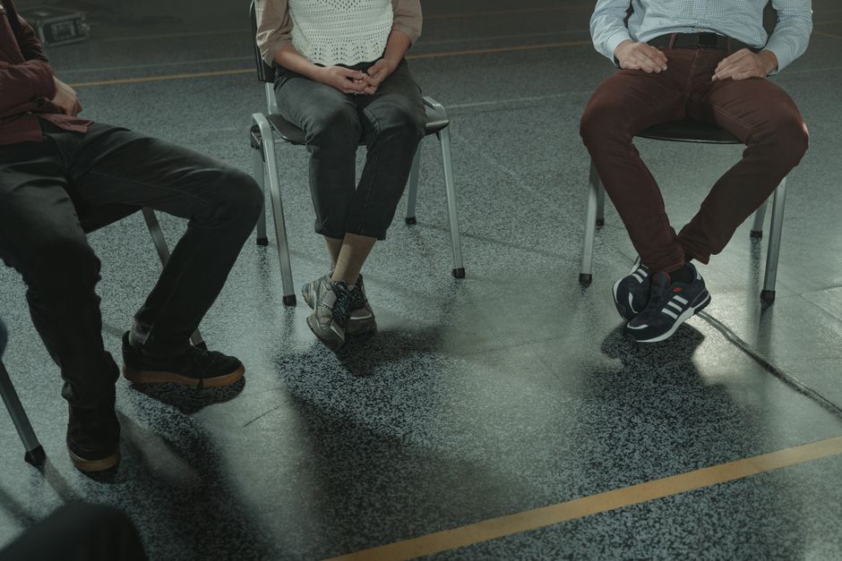 A group of three adults sitting in chairs during a discussion or support session indoors.