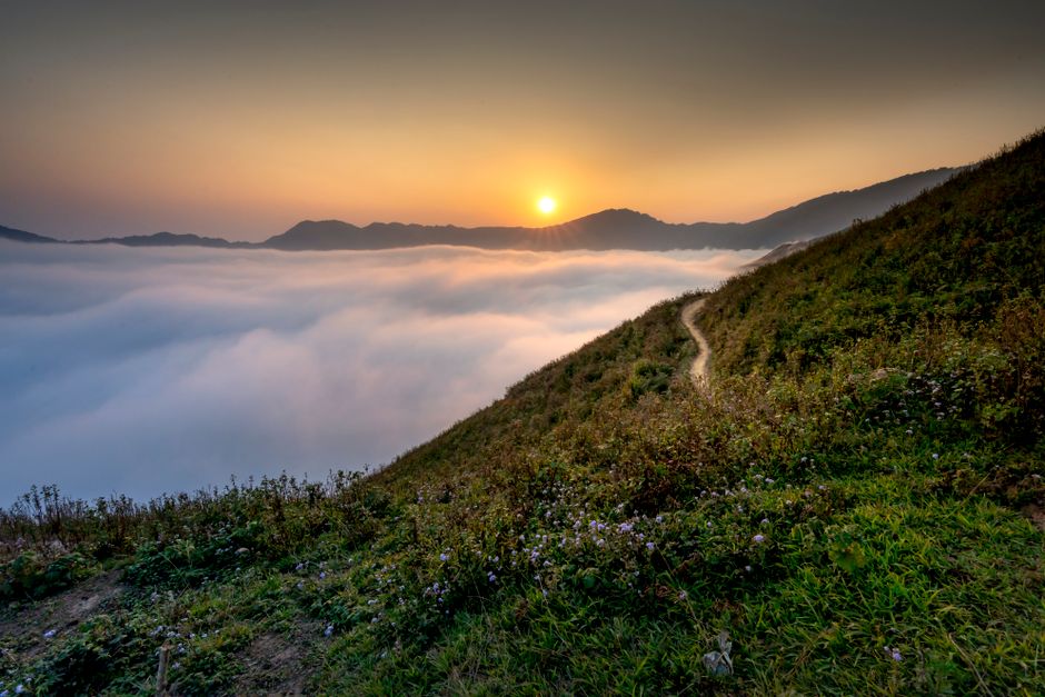 Stunning sunrise over mountains with a sea of clouds and a winding hill path.