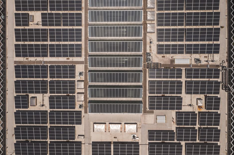 Mind reading A high-angle drone shot capturing a grid of solar panels on a large industrial rooftop, showcasing renewable energy.