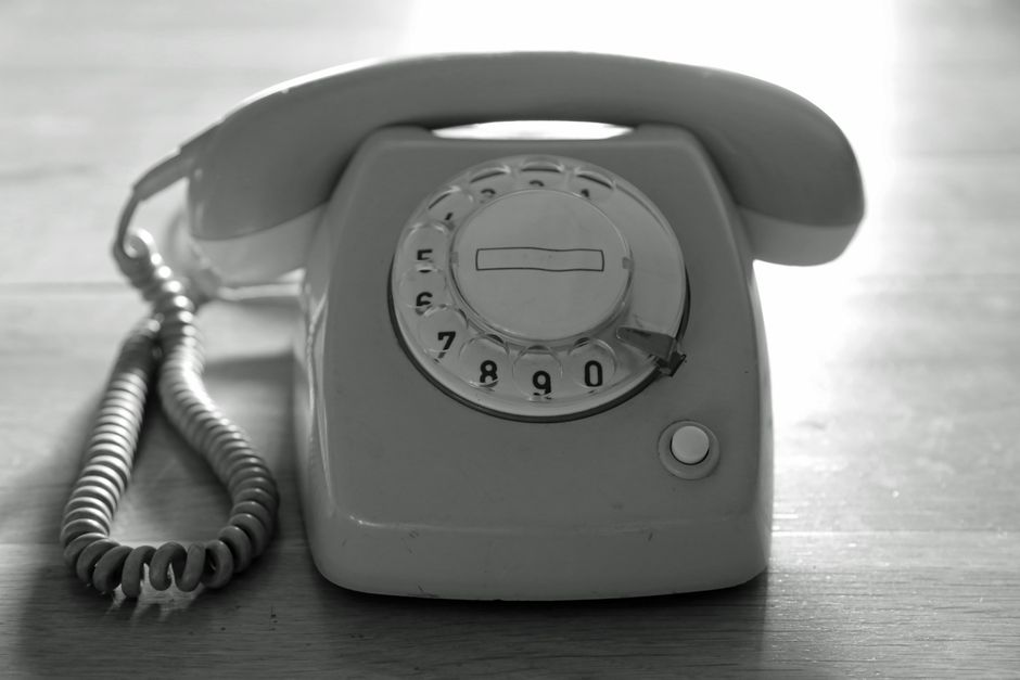 High contrast black and white image of a vintage rotary phone on a wooden surface emphasizing nostalgic communication.