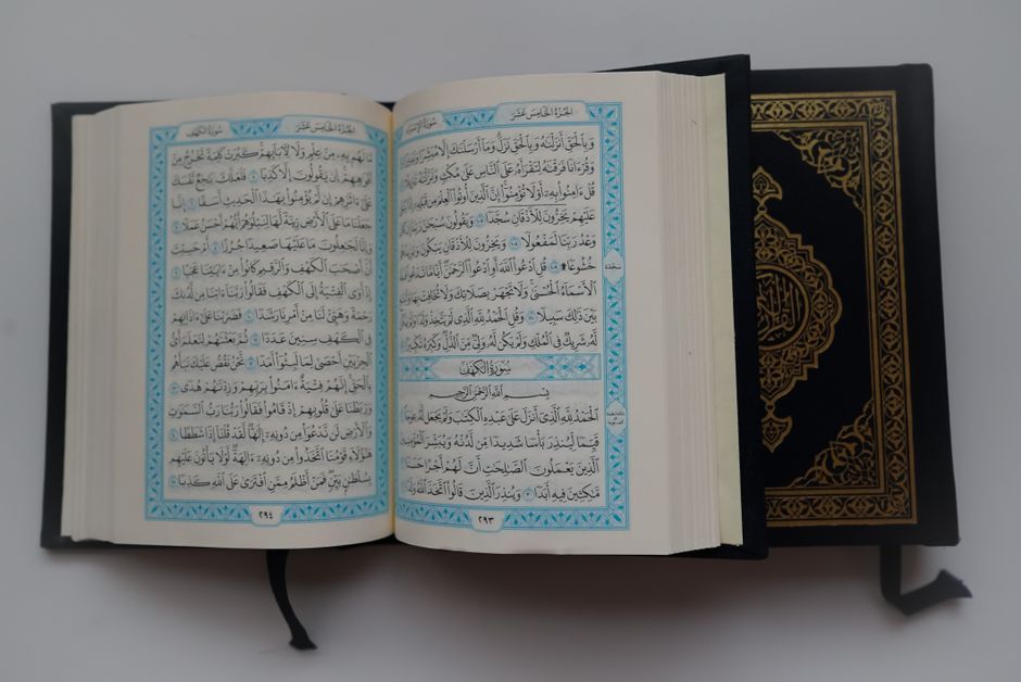 Close-up of an open Quran showcasing Arabic script and decorative cover on a gray surface.