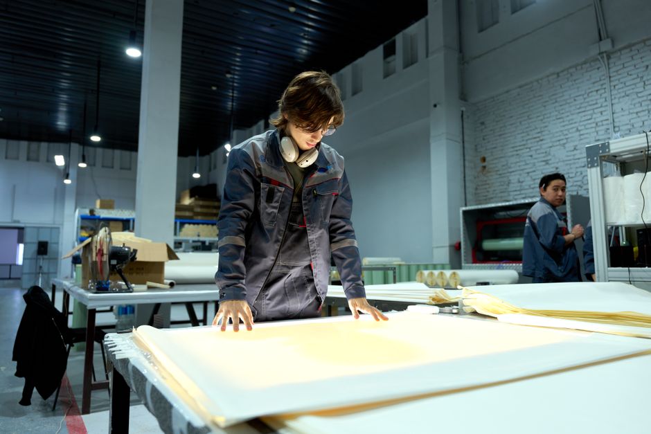 Worker in uniform examining sheets in a brightly lit factory environment, focusing on quality.