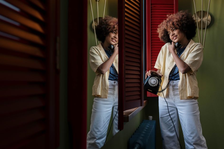 A cheerful young woman with afro hair using a vintage rotary phone, reflecting joy and nostalgia.
