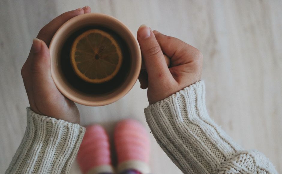 A warm cup of lemon tea held in cozy hands on a winter morning.