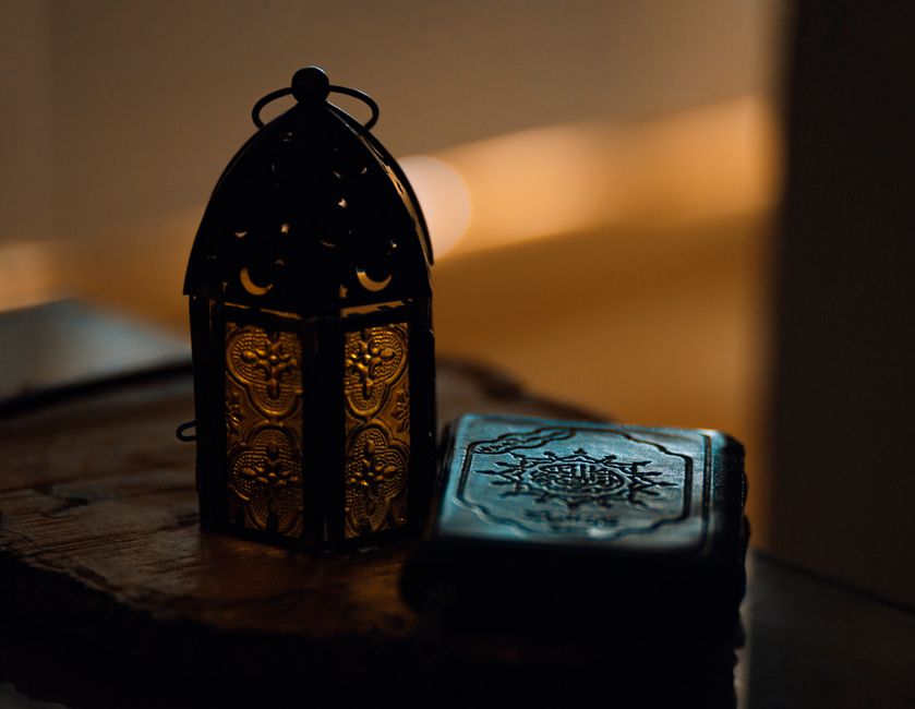 Dimly lit lantern and Quran on table, symbolizing Ramadan's spiritual ambiance.